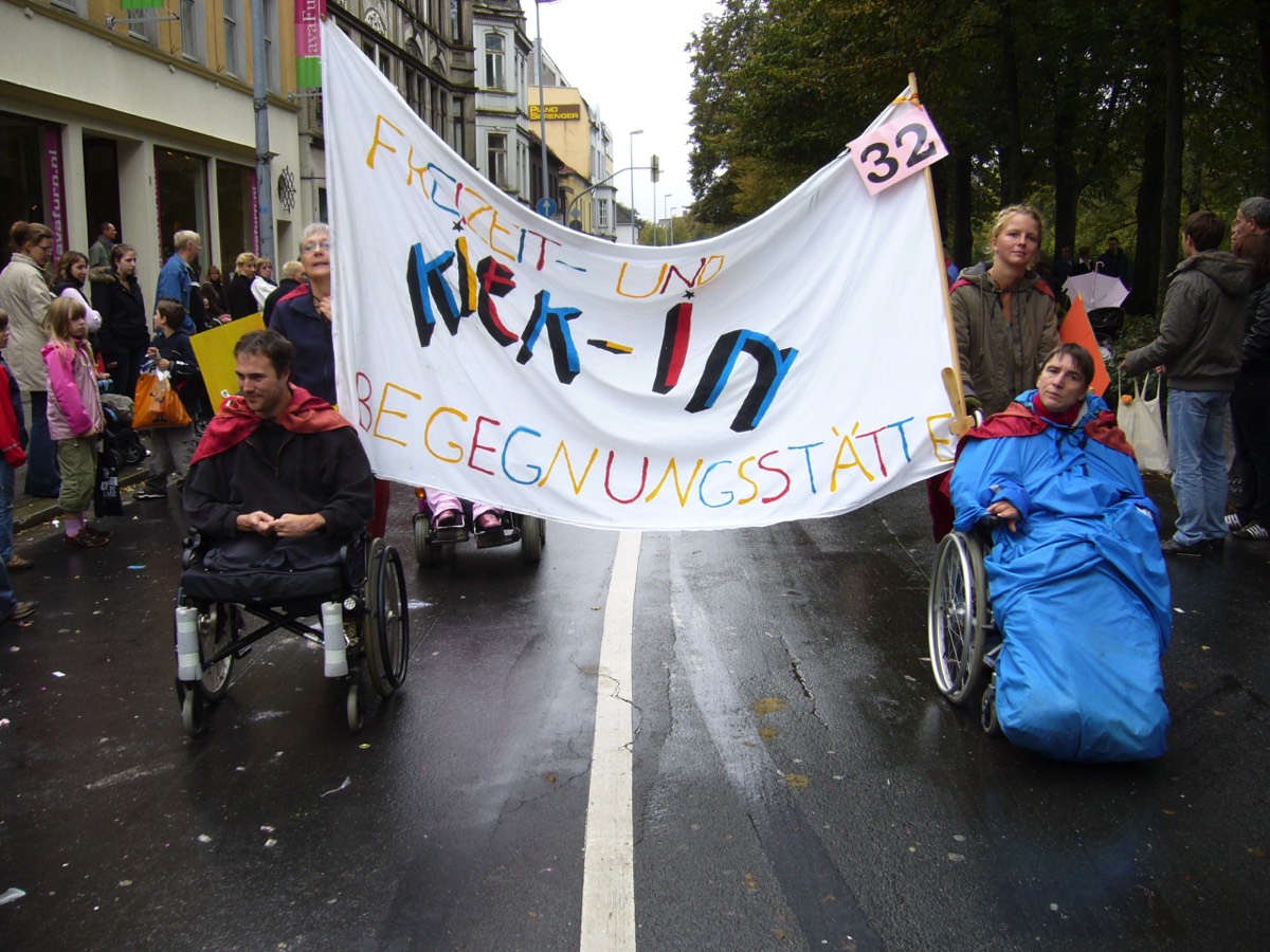 Auf dem 3. Bild sieht man Menschen, die im Rollstuhl geschoben werden und ein großes Banner mit KIEK-IN halten. Sie gehen beim Kramermarktsumzug mit.