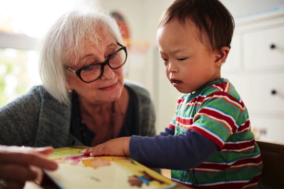 Auf dem 9. Bild sieht man eine Ã¤ltere freiwillige Frau, die sich zusammen mit einem kleinen Jungen ein Bilderbuch anschaut.